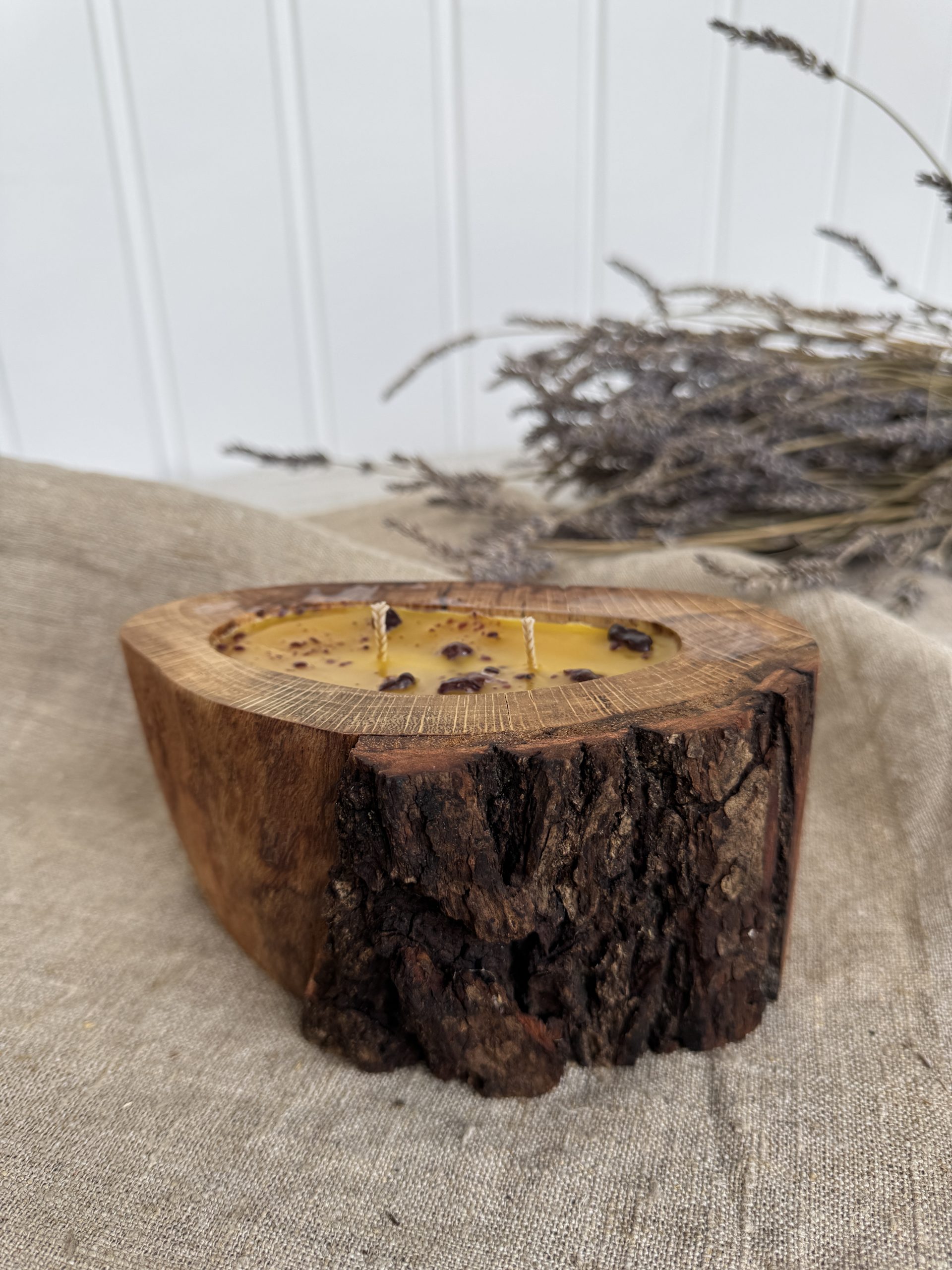 Handmade natural beeswax candle with propolis in rustic oak wood vessel with preserved bark texture