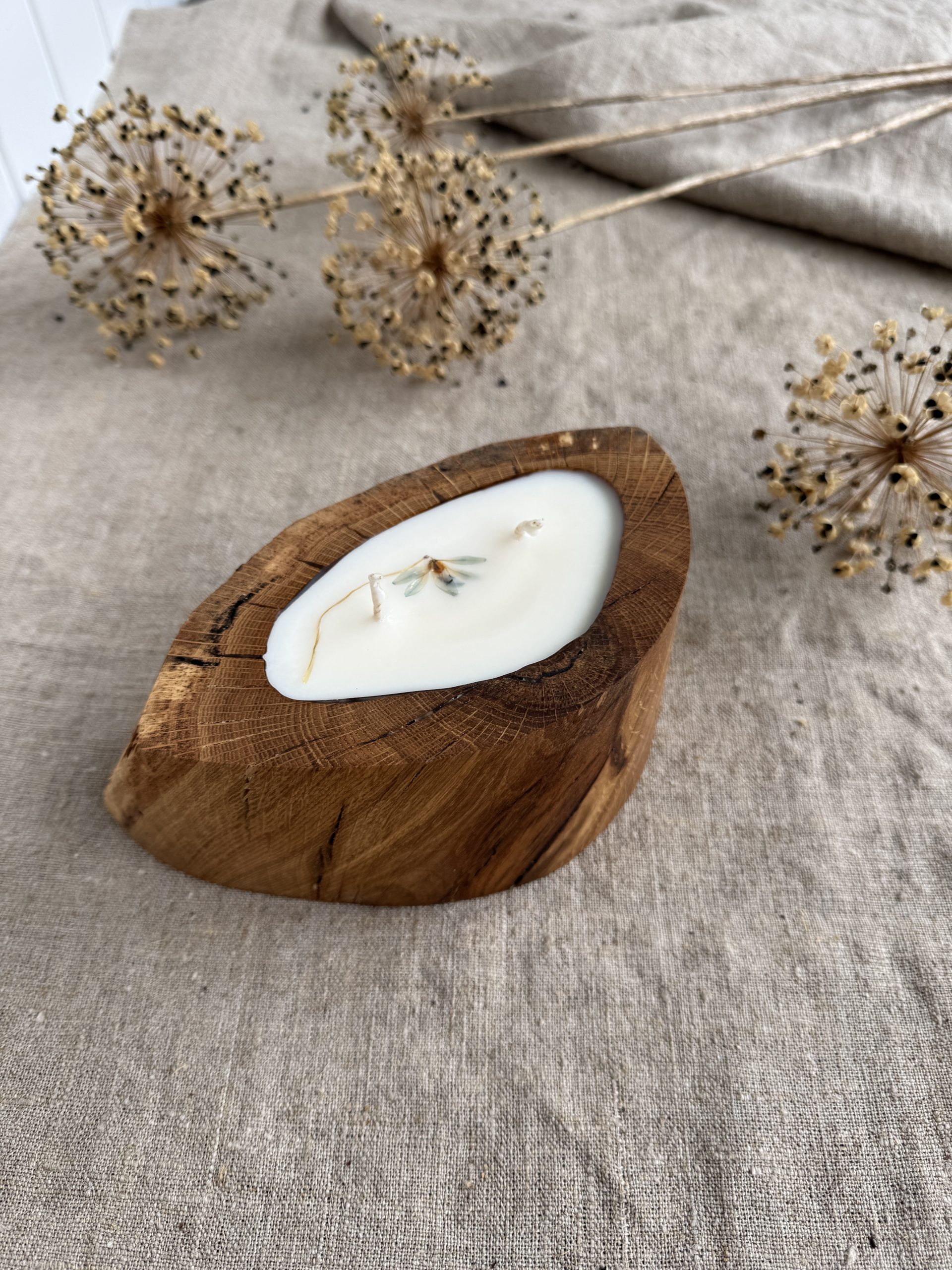 Handmade vanilla scented candle in a rustic oak wood vessel with natural wood grain and botanical decoration